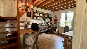 A rustic room with exposed wooden beams, a bookshelf, a desk, a chair, and a window.