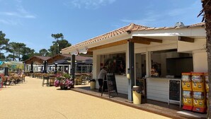 An outdoor seating area with tables and chairs, a covered seating area with a menu board, and a vending machine. - Bungalow between nature and ocean at Le Ferret, a 4* resort with aquatic areas (Lège-Cap-Ferret)