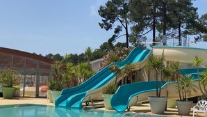 A swimming pool with two slides, surrounded by potted plants and a clear sky. - Bungalow between nature and ocean at Le Ferret, a 4* resort with aquatic areas (Lège-Cap-Ferret)