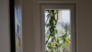Ein Schlafzimmer mit einem Bett, einer Tür, die auf einen Balkon mit Pflanzen führt, und einem an der Wand hängenden Gemälde.