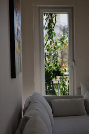 A bedroom with a bed, a door leading to a balcony with plants, and a wall-mounted painting.