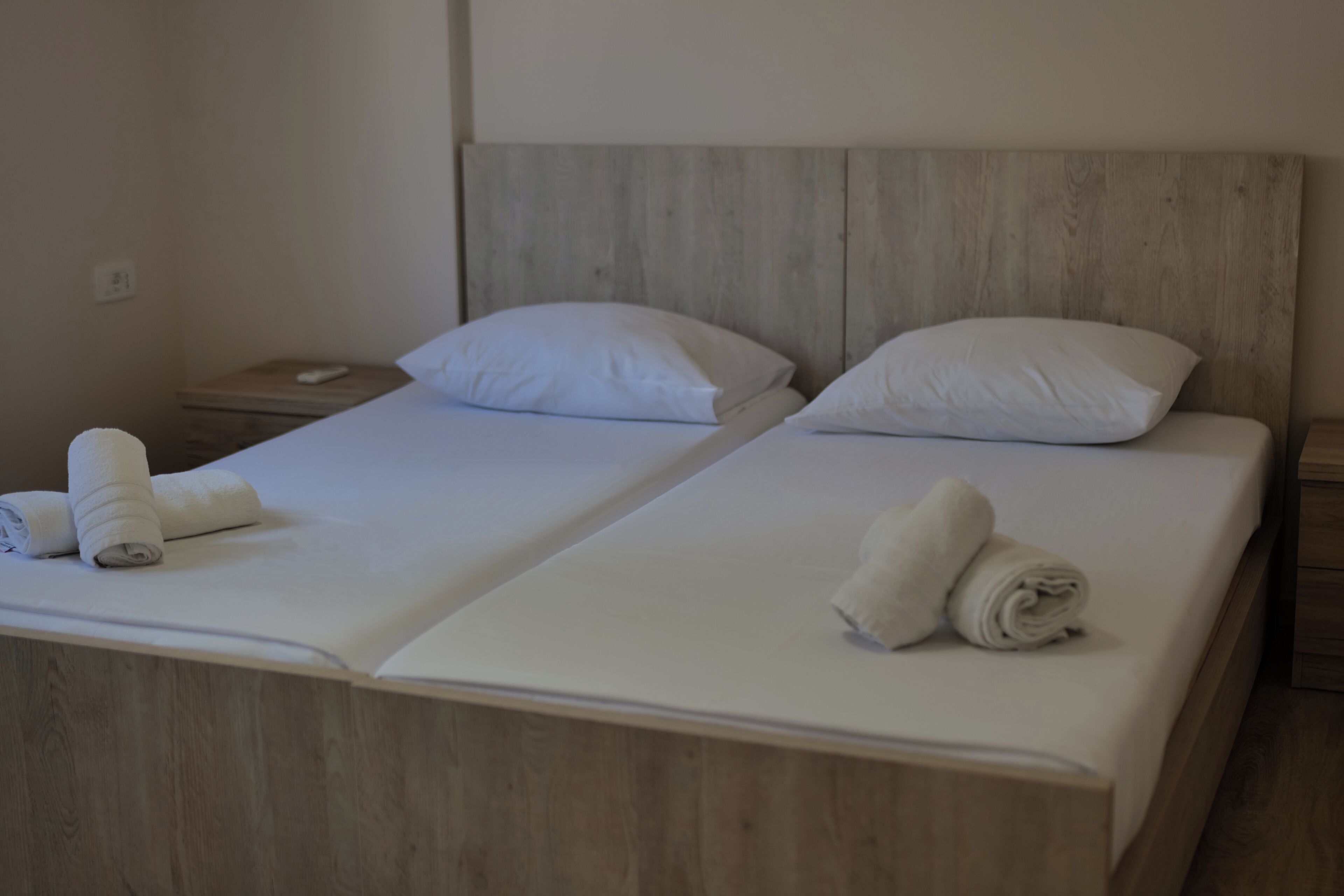 Two single beds with wooden headboards, white bedding, and rolled towels on each bed.