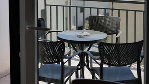 Ein Balkon mit Tisch und Stühlen, Blick auf das Meer und angrenzende Gebäude.