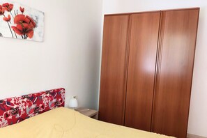 Un dormitorio con cama, un armario de madera, una mesita de noche con lámpara y un cuadro con motivos florales en la pared.