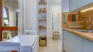 Moderni keittiö, jossa on valkoiset kaapit, puinen työtaso ja integroitu pesuallas. Siellä on hyllyjä, joilla on keittiötarvikkeita, sekä pieni puinen jakkara.