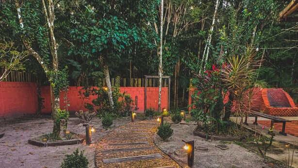 Un sendero serpentea por un jardín con un muro rojo y árboles.