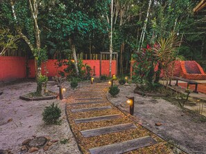 A pathway leading through a garden with a red wall and trees. - Riverside Ranch and Open-Fire Grill in Iguape (Iguape)