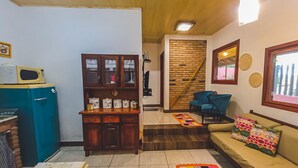 Un salón con techo de madera, un refrigerador azul, un mueble de madera, un sofá con cojines coloridos y una alfombra estampada.