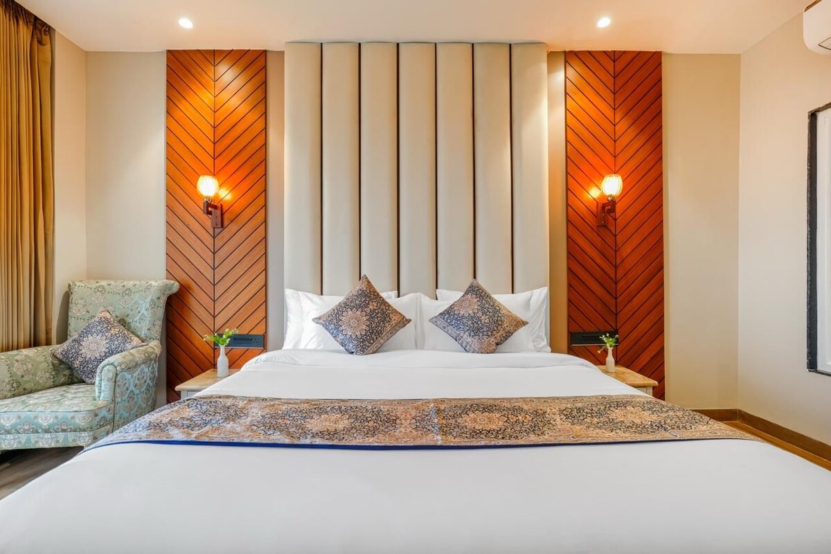 A hotel room with a bed, two wall-mounted lights, a nightstand, a chair, and a decorative wall panel.