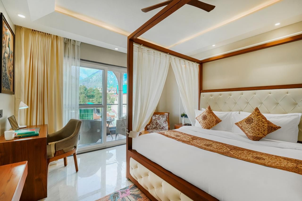 A bedroom with a large bed, a desk, a chair, and a balcony with a view.
