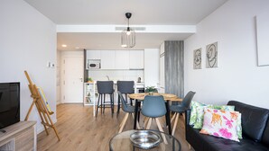 A modern living room with a dining area, a black leather sofa, a glass coffee table, and a wooden easel. - RivasCenter Apartment (Rivas-Vaciamadrid)