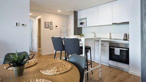 A modern kitchen with white cabinets, a microwave, and a dishwasher. There is a dining area with a table, chairs, and a potted plant. - RivasCenter Apartment (Rivas-Vaciamadrid)