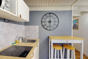 A modern kitchen with a built-in stove, a sink, and a wooden table with two stools. - Charming T1 Nantes center near tramway & train station (Nantes)