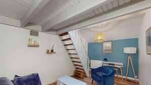 Un salon moderne avec un escalier, un fauteuil bleu, une console blanche et un bureau avec une lampe.