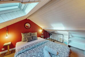 A bedroom with a sloped ceiling, a bed with patterned bedding, a round mirror, and a small table with a lamp. - Charming one-bedroom apartment in downtown Nantes, near the tram and train station (Nantes)