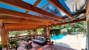 A wooden deck with a sofa and potted plants, overlooking a swimming pool.