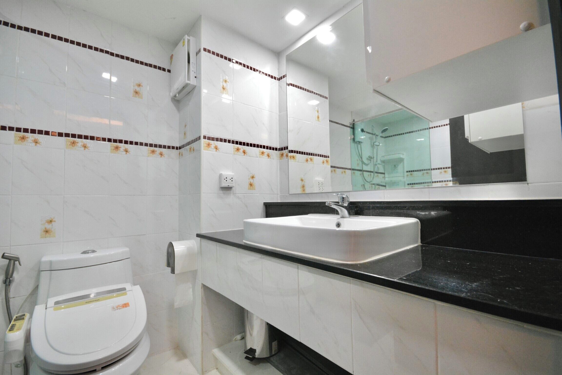 Une salle de bain moderne avec des toilettes blanches, un lavabo doté d’un plan de travail noir et un miroir au-dessus du lavabo.