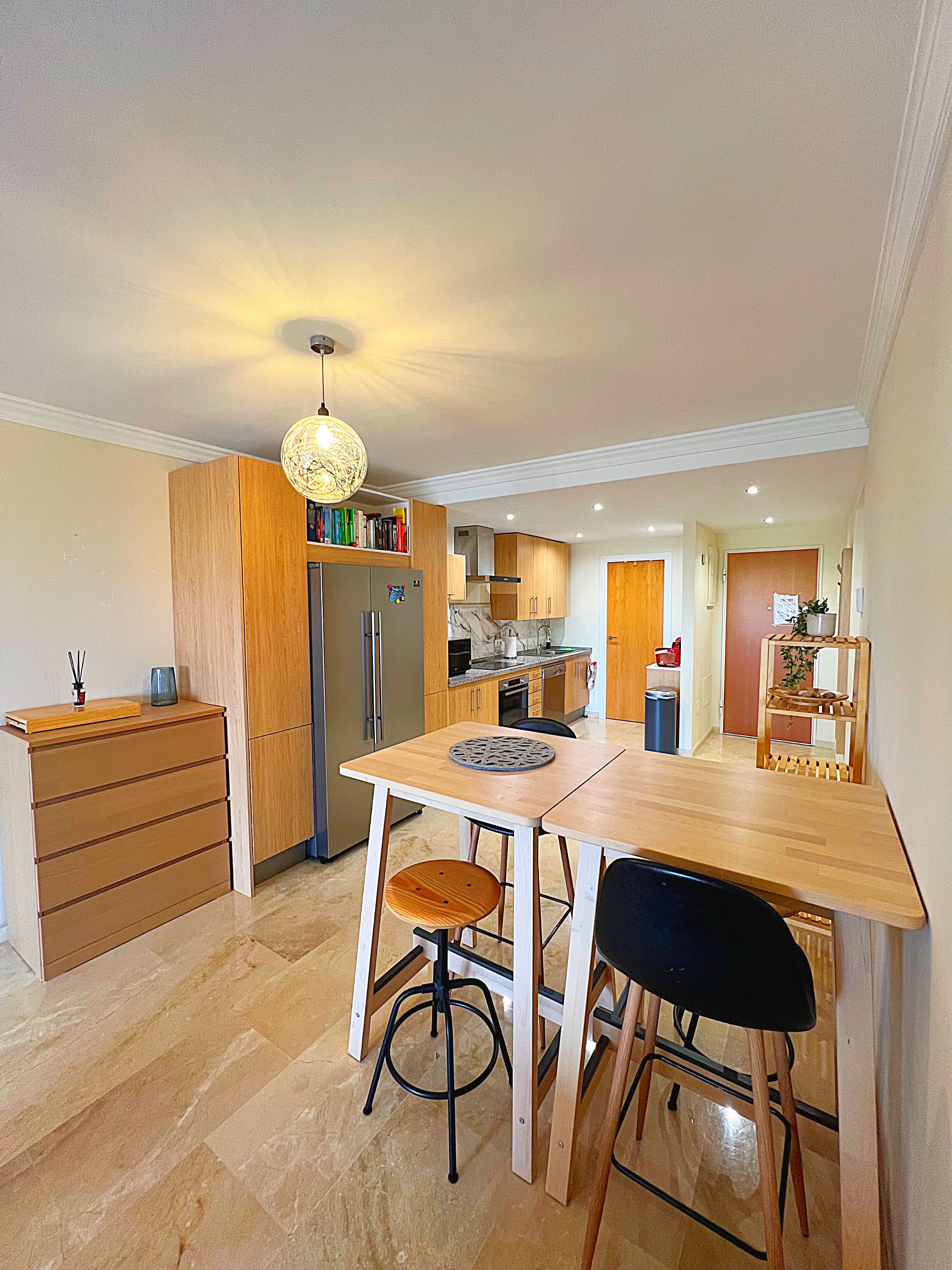 Une cuisine moderne avec des meubles en bois, un réfrigérateur encastré et un coin repas comprenant une table et des chaises.