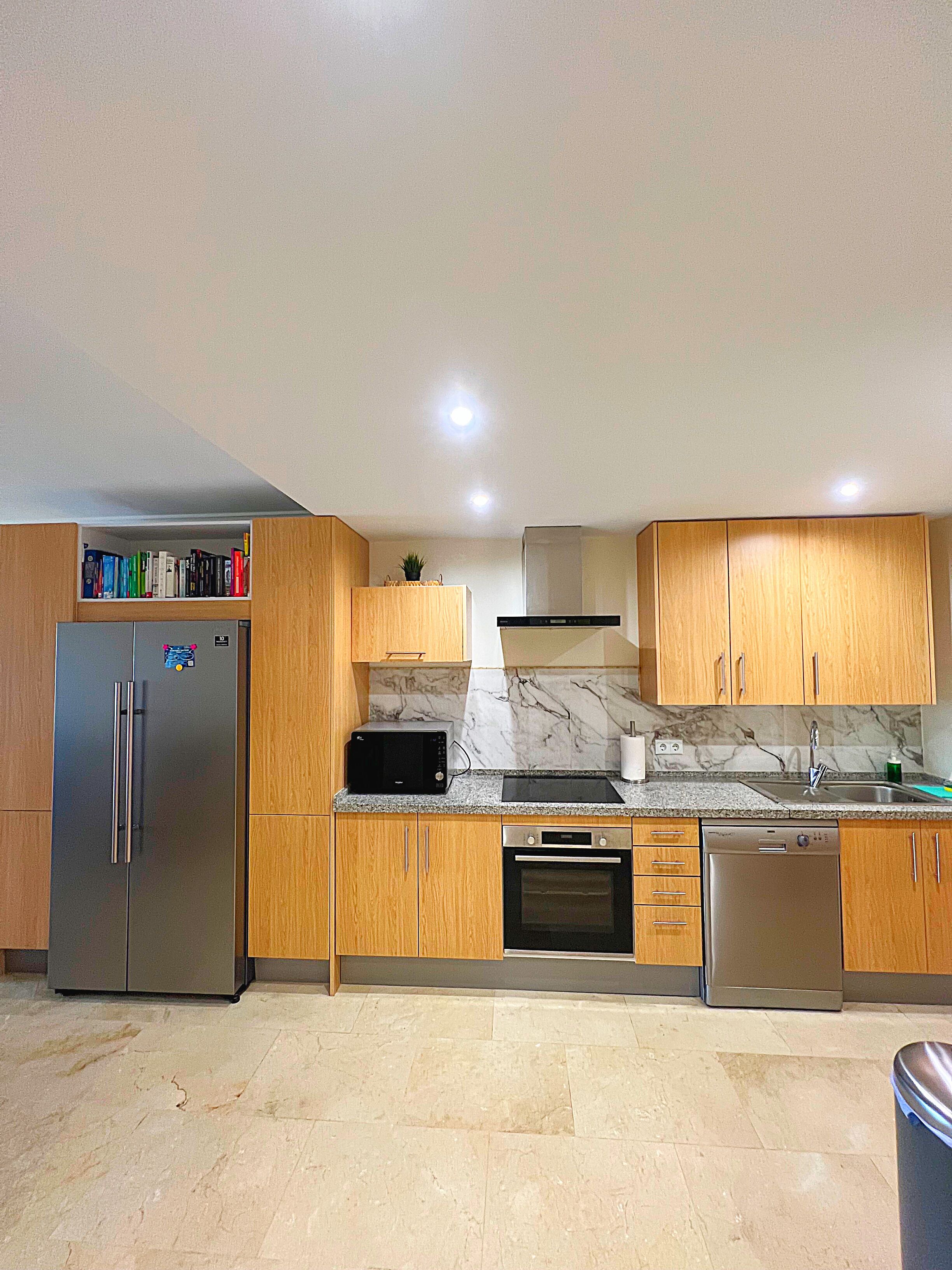 Una cocina moderna con gabinetes de madera, un refrigerador de acero inoxidable, microondas, horno y lavavajillas.