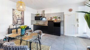 Une cuisine moderne avec un poêle noir, un luminaire suspendu et un coin repas comprenant une table en verre et des chaises rembourrées.