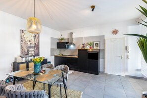 Una cucina moderna con piano cottura nero, una lampada a sospensione e un'area pranzo con tavolo in vetro e sedie imbottite.