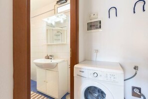 A compact bathroom with a white sink, a mirror, and a front-loading washing machine. - Via Roma Apartment (Stresa)