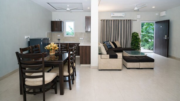 Una sala de estar moderna con comedor, un conjunto de sofás y una cocina al fondo.