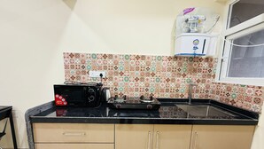 A compact kitchen with a microwave, kettle, and a water dispenser on the countertop. - 1BR Service Apart Parel 3405 Near TMH By Florastays (Mumbai)