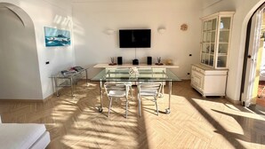 Un comedor moderno con una mesa y sillas de vidrio, un televisor de pantalla plana en la pared y un armario con puertas de cristal.