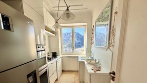 Cocina compacta con refrigerador, estufa y lavaplatos. Se ve una ventana con vistas a montañas.