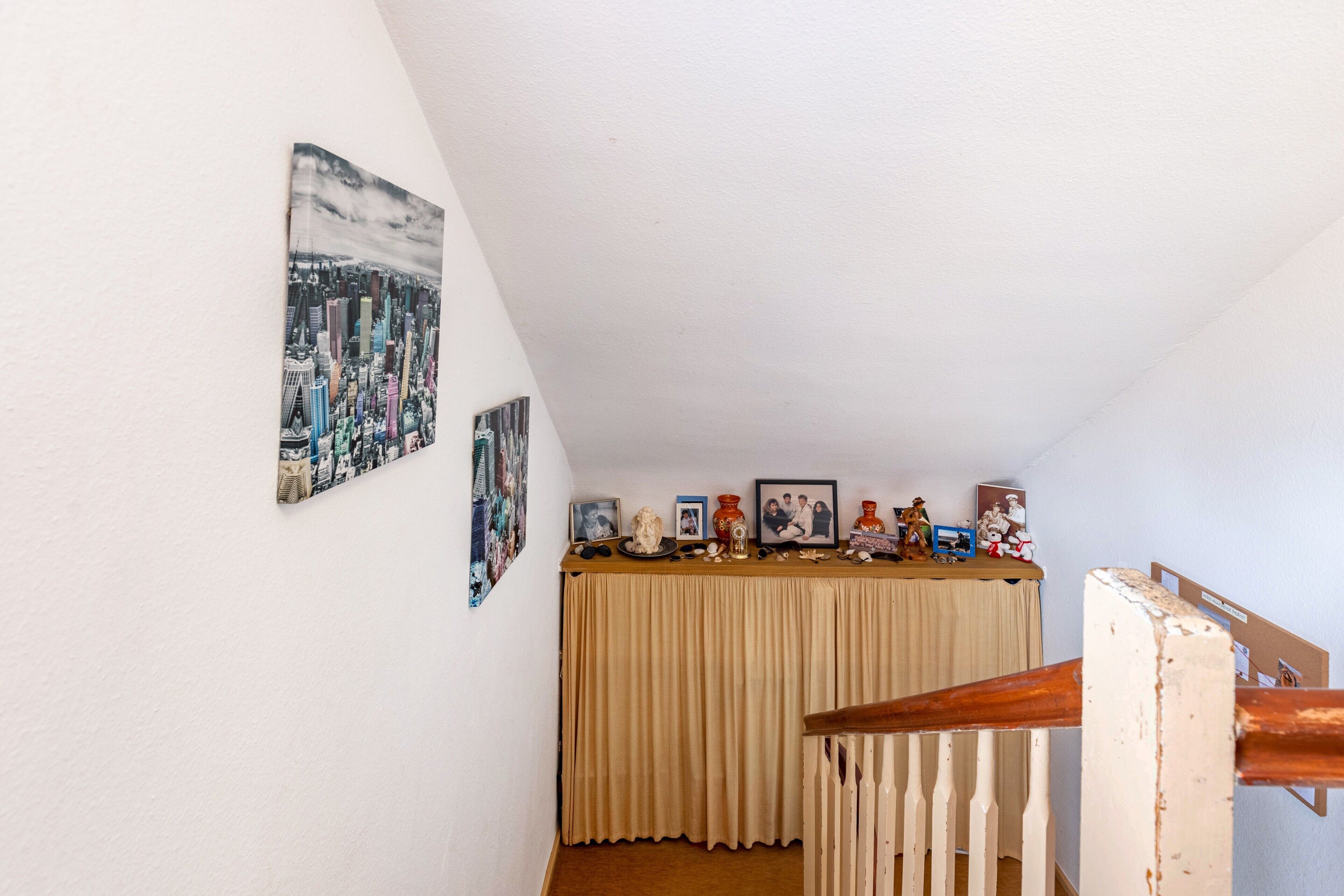 A room with a staircase, a table with various items, and two framed pictures on the wall.