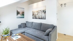 Uma sala de estar moderna com um sofá cinzento, uma mesa de centro de madeira e duas obras de arte penduradas na parede.