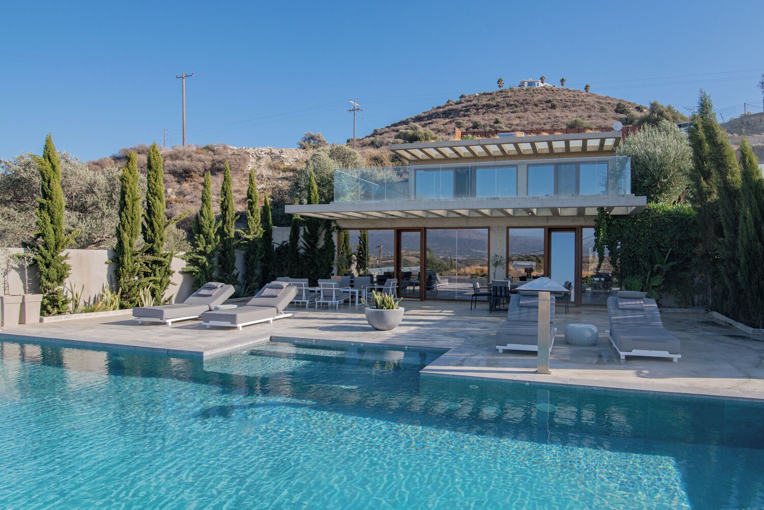 A modern house with a pool, outdoor seating, and a view of a hill.