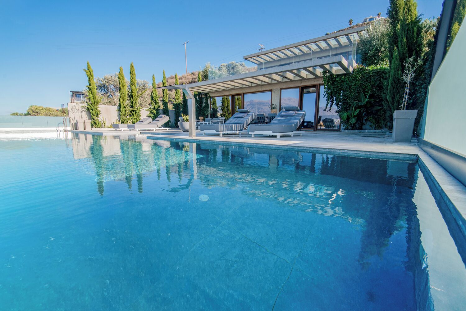 Una piscina azul cristalina con sillones de descanso y una pérgola.