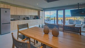 A modern kitchen with wooden cabinets, a dining table with chairs, and a view of mountains through large windows. - Marnos Grand Villa (Faistos)