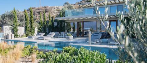 Une maison moderne dotée d’une piscine, d’un espace salon extérieur et offrant une vue sur un paysage vallonné.