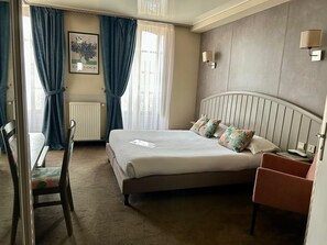 Une chambre d’hôtel avec un lit, une chaise, une table de chevet, une lampe et un radiateur.