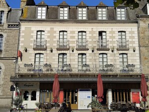 A building with multiple windows and balconies, a ground-floor entrance with a sign reading 'LE LOU EVILLE,' and outdoor seating with umbrellas. - Marguerite (Dinan)