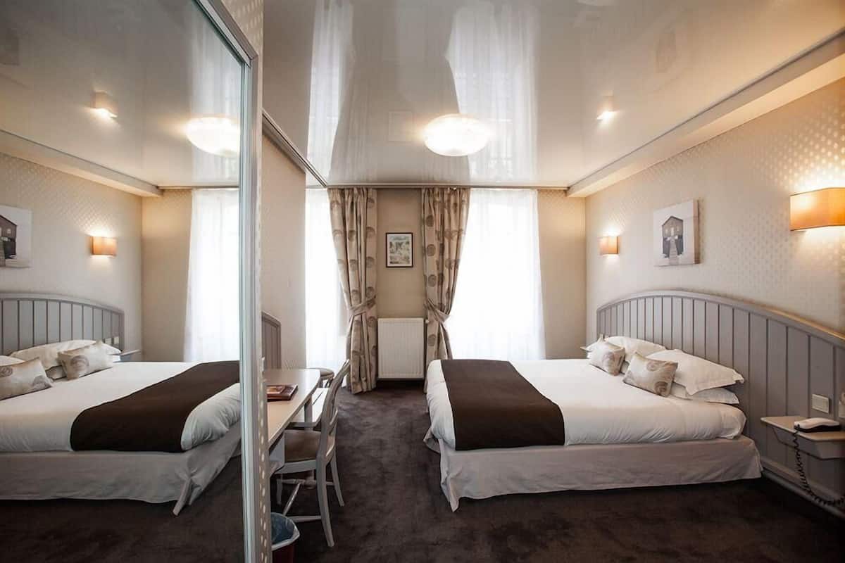 Une chambre d’hôtel avec deux lits, un bureau, une chaise et un miroir.