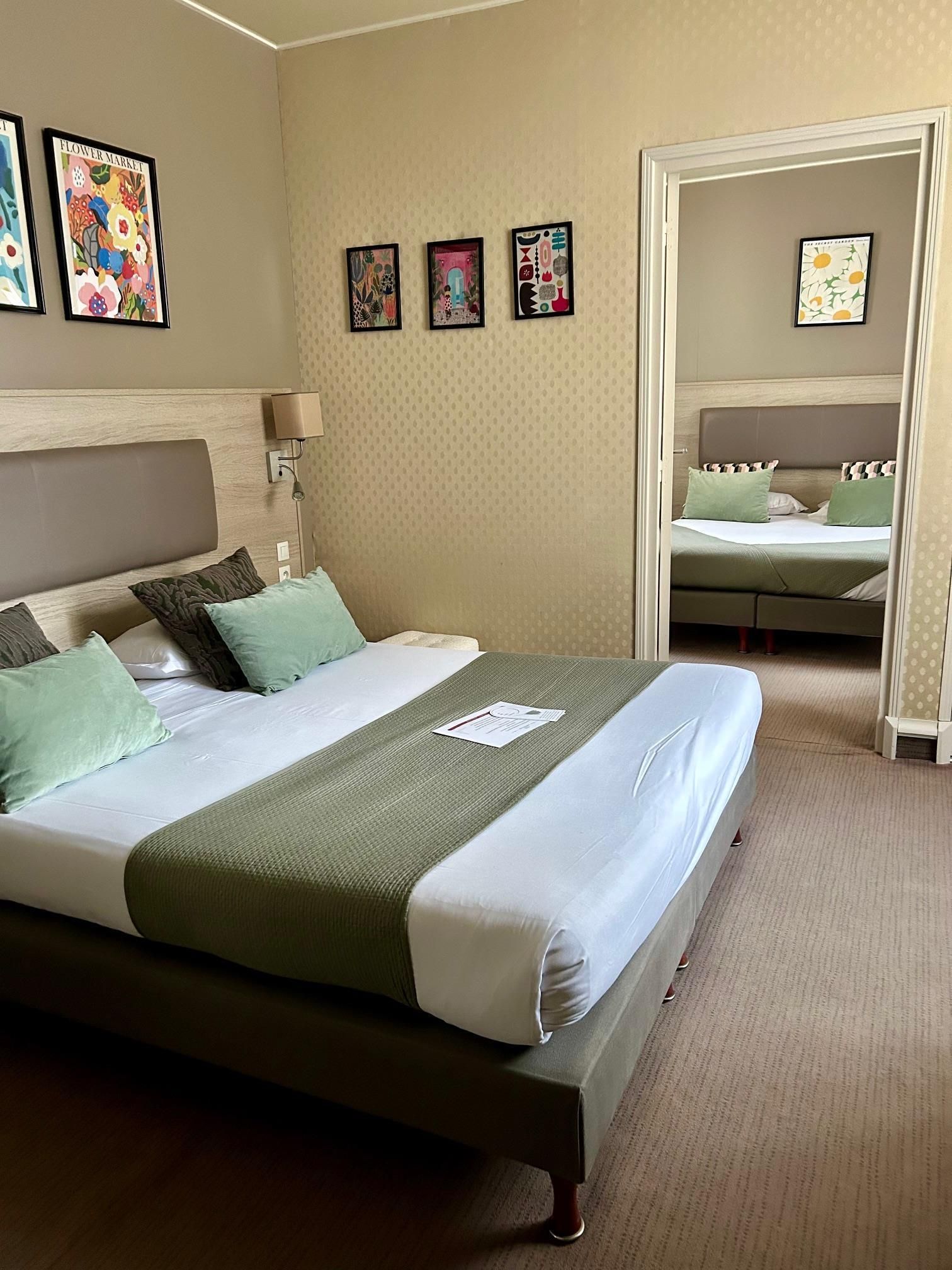 A hotel room with a large bed, a smaller bed, a nightstand, a lamp, and four framed pictures on the wall.