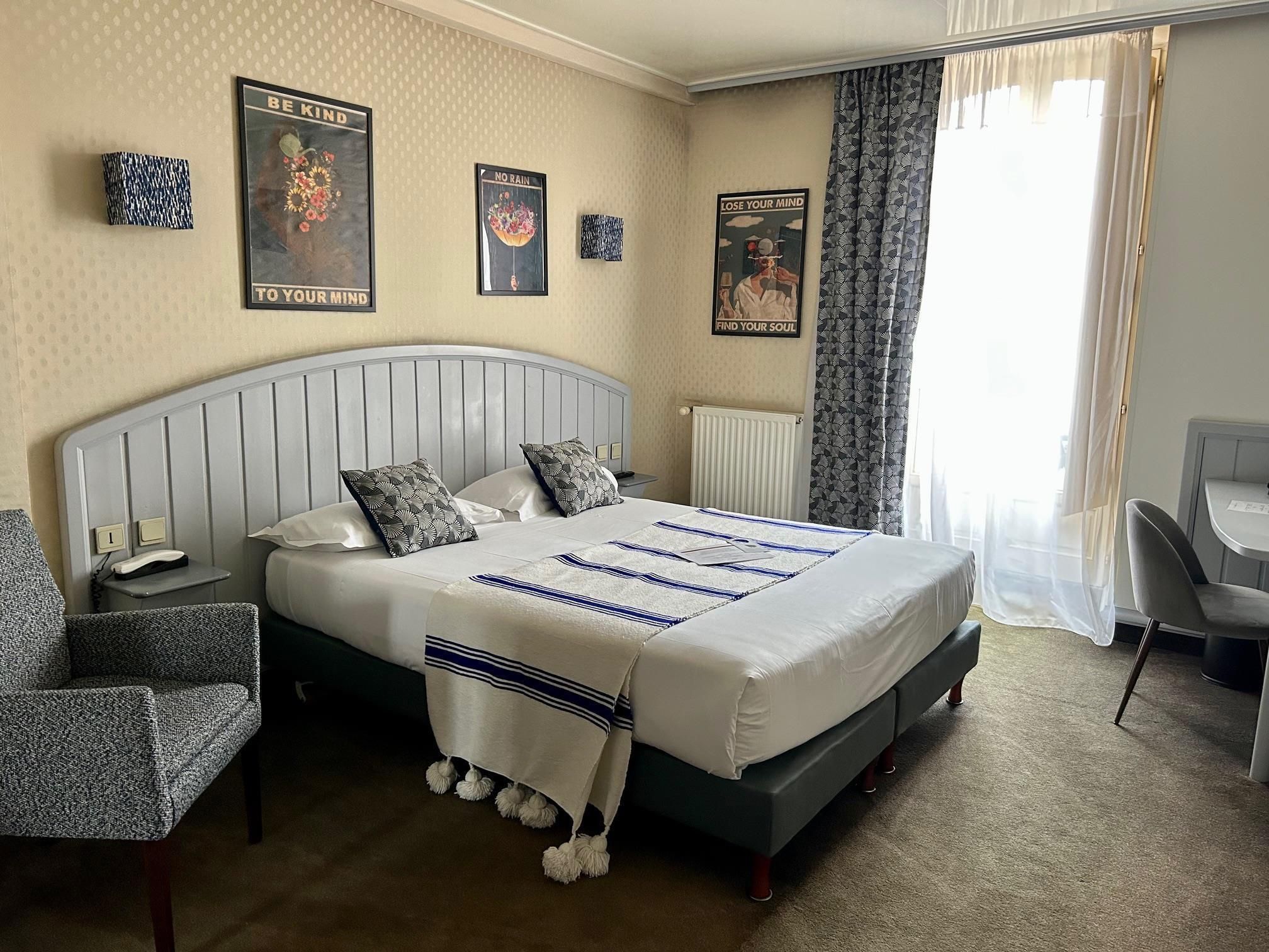 A hotel room with a bed, a chair, a desk, and a window with curtains.