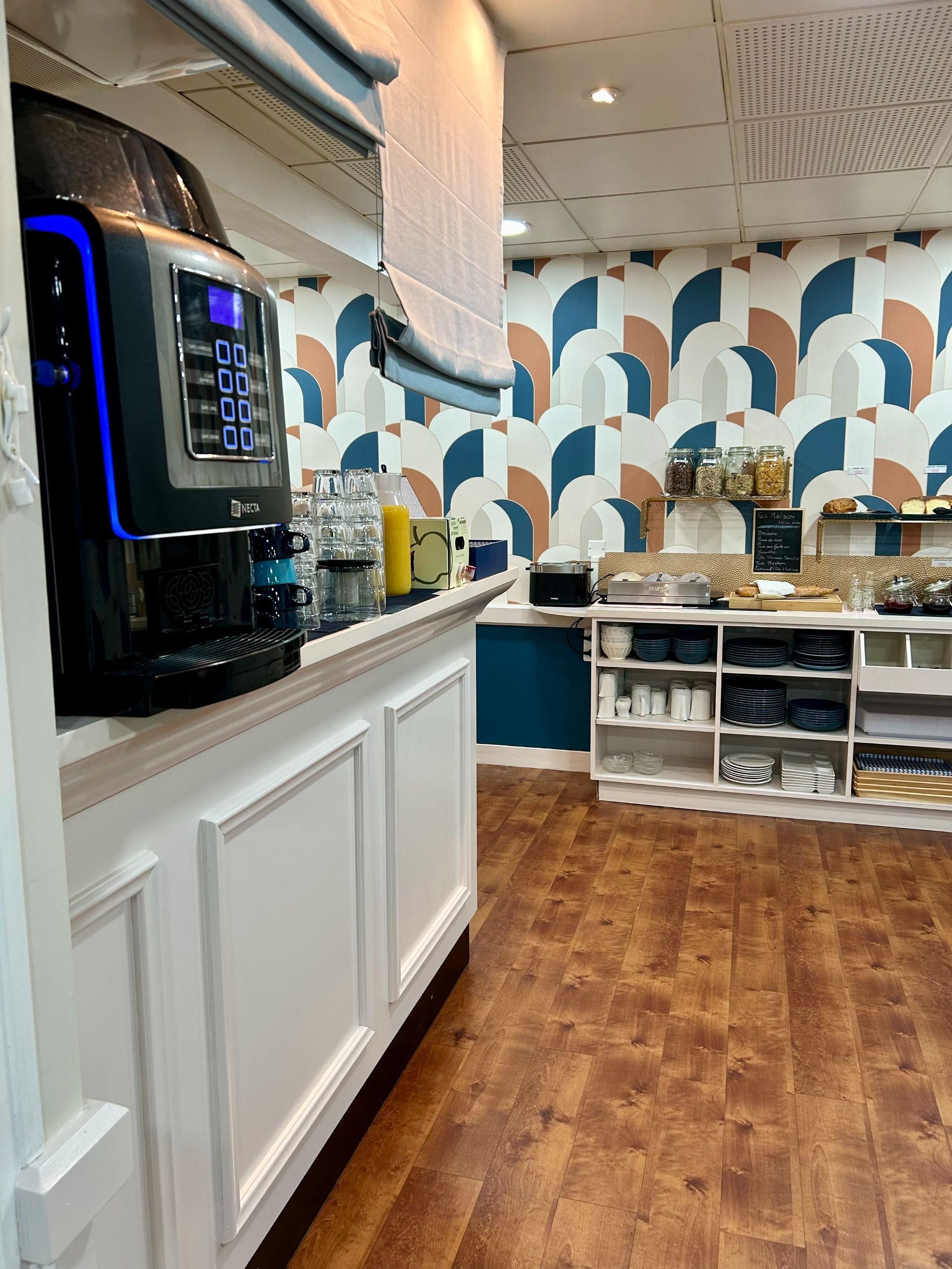 Un café moderno con una máquina de café, estantes con frascos y una pared con estampado.