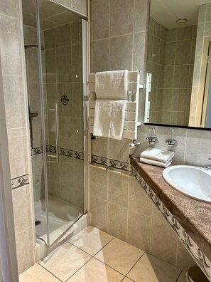 A bathroom with a glass-enclosed shower, a sink with a marble countertop, and a towel rack with folded towels. - Marguerite (Dinan)