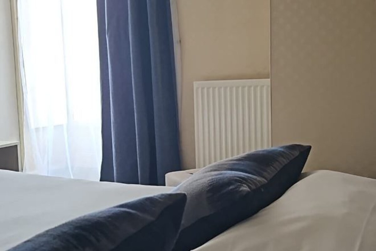 Hotellihuone, jossa on sänky, ikkuna verhoilla ja patteri.