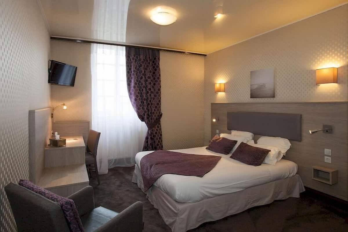 Une chambre d’hôtel équipée d’un lit, d’un bureau, d’une chaise, d’une télévision et d’une fenêtre avec des rideaux.