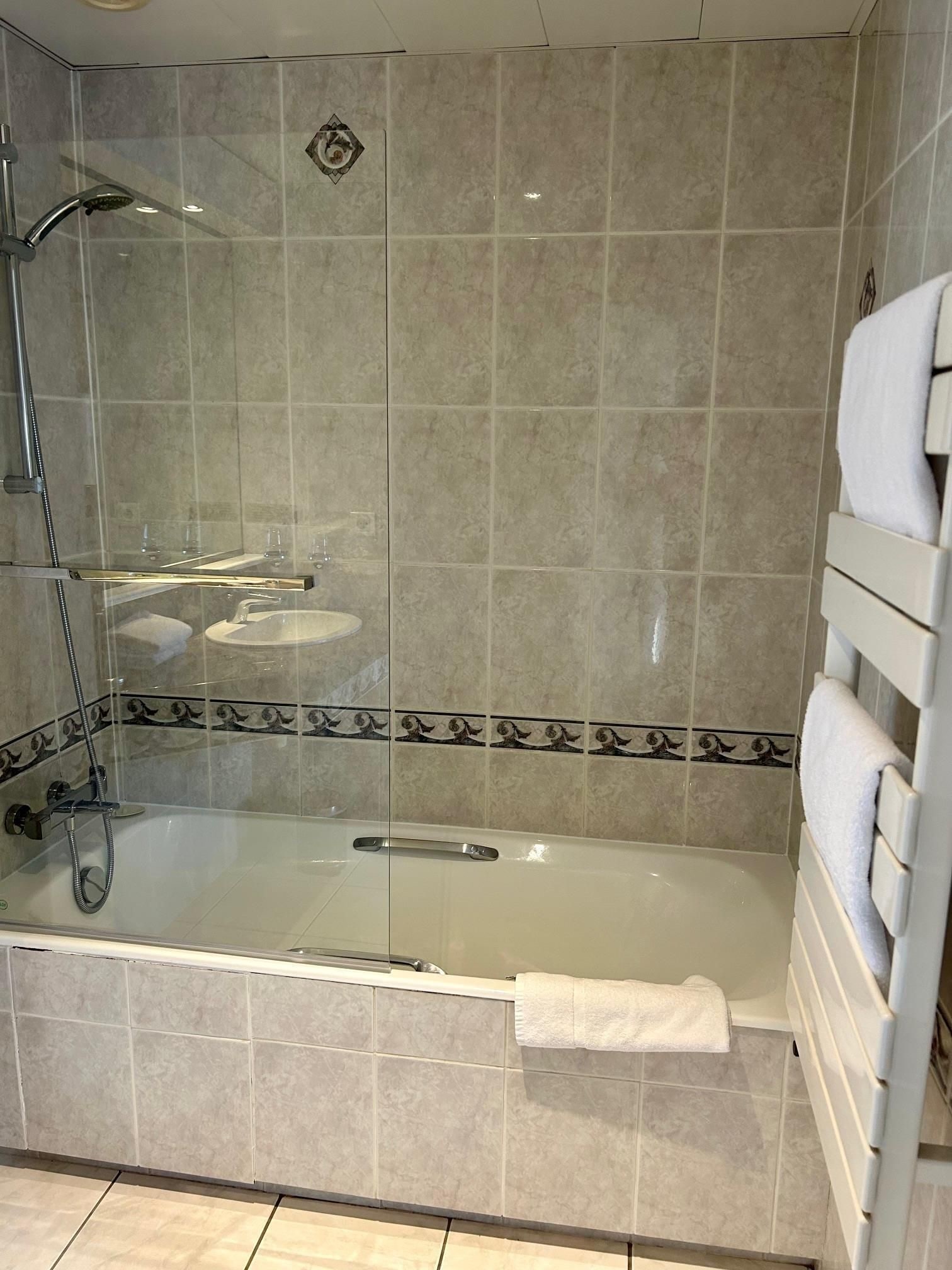 A glass-enclosed shower with a handheld showerhead, a built-in seat, and a towel rack.
