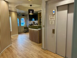 A hotel corridor with a reception desk, a door with a lock, and a window with a view. - Marguerite (Dinan)
