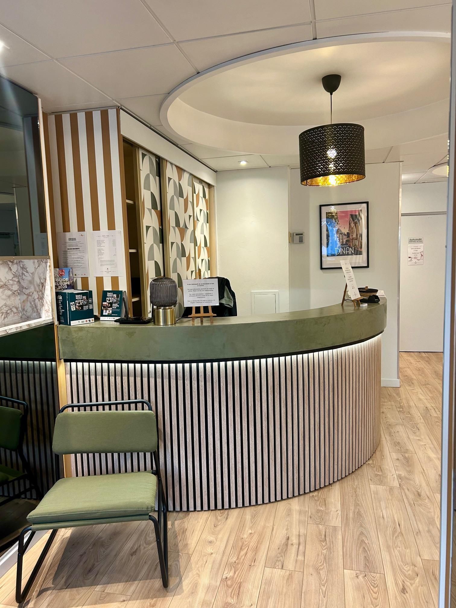Un área de recepción con un mostrador curvo, una silla verde y un papel tapiz estampado.