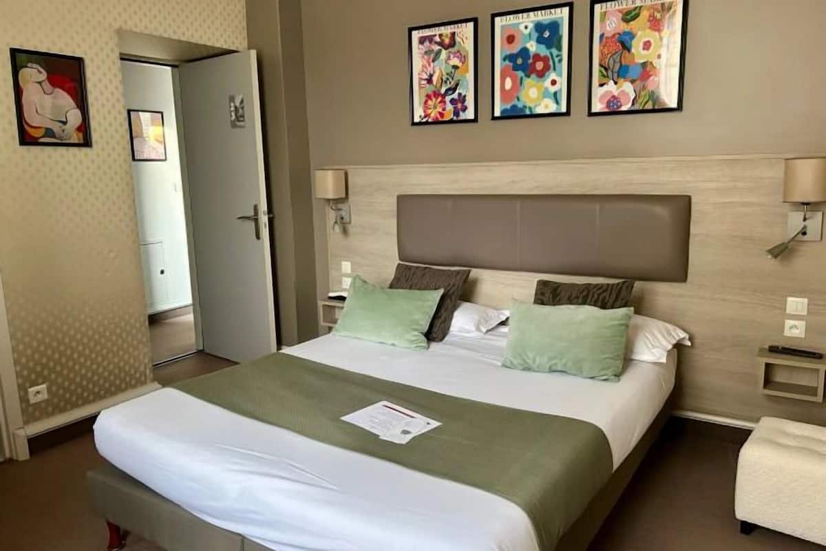 Une chambre d’hôtel comprenant un lit, une table de chevet, une commode, une porte et des œuvres d’art mural.