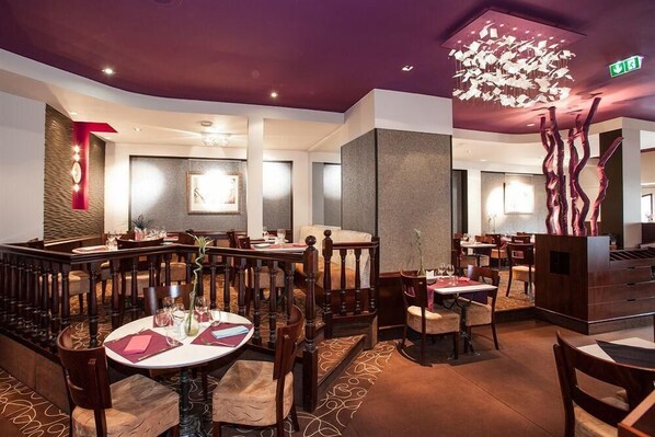 Ein Restaurant mit runden Tischen, Holzstühlen und einer modernen Pendelleuchte.
